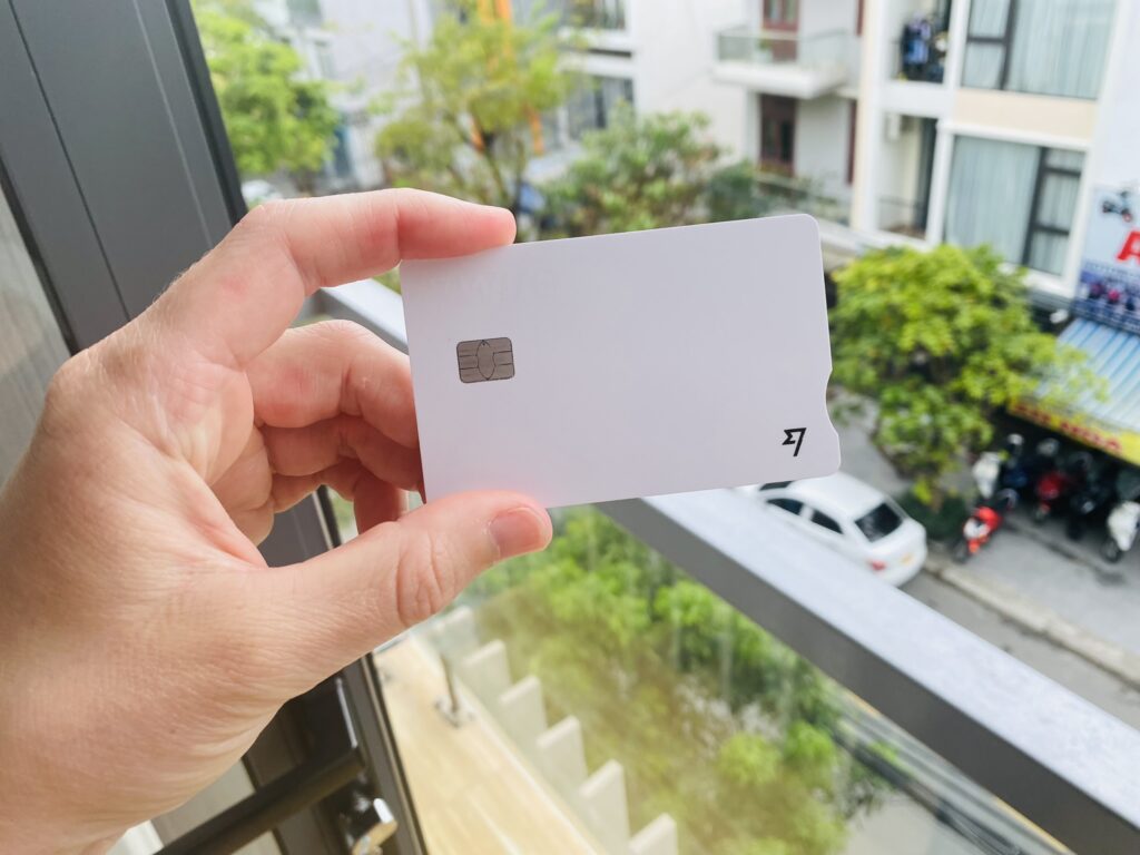 A white Wise debit card being held up in front of some Vietnamese buildings